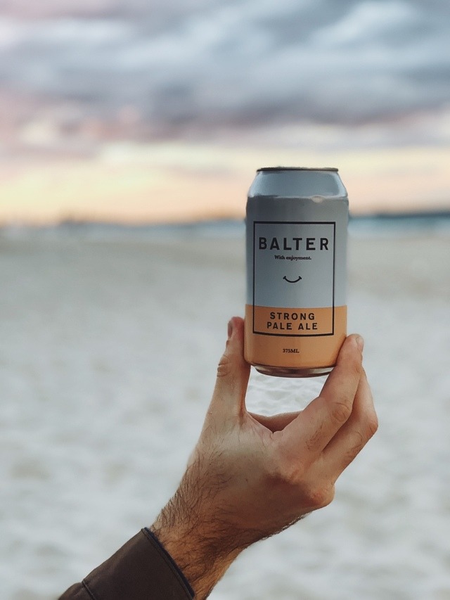 photo of beer being held in front of beach